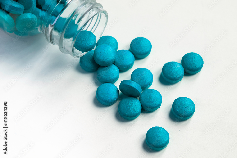 Turquoise blue pills and tablets spilling out from glass pill bottle on white background Turquoise blue pills and tablets spilling out from glass pill bottle on white background