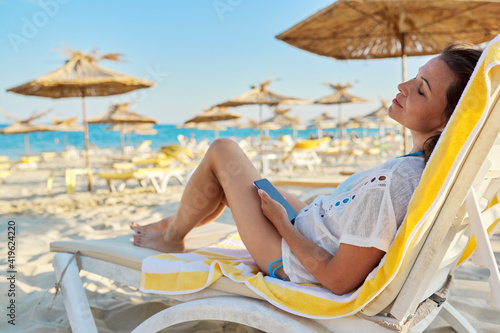 Relaxing mature woman sitting on sun lounger on the beach