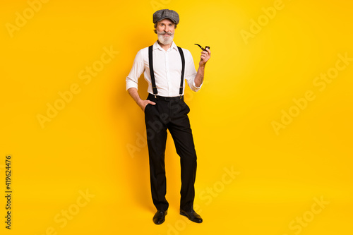 Full length photo of mature man happy positive smile hold pipe smoker tobacco isolated over yellow color background