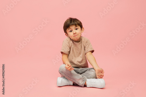 Dreaming, doubtfull. Happy, smiley little caucasian boy isolated on pink studio background with copyspace for ad. Looks happy, cheerful. Childhood, education, human emotions, facial expression concept