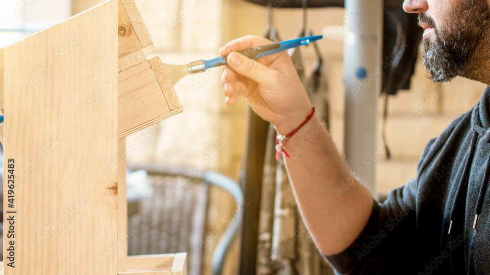 Obraz premium Bearded man doing DIY at home, painting wood with brush.
