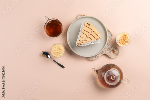 A piece of cheesecake on a plate with a teapot and a cup of tea on a colored background. A delicious dessert for a birthday and holiday.