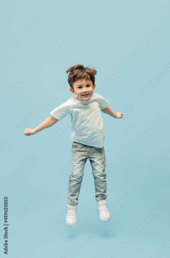 Jumping high. Happy, smiley little caucasian boy isolated on blue studio background with copyspace for ad. Looks happy, cheerful. Childhood, education, human emotions, facial expression concept.