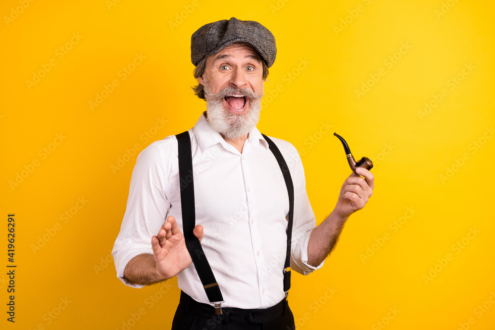 Photo portrait of surprised gentleman in shirt suspenders keeping wooden pipe smiling overjoyed isolated bright yellow color background