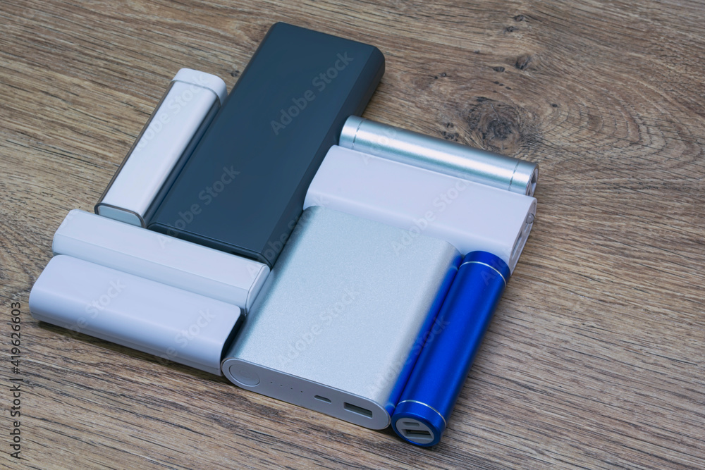 Set of power banks of different sizes on a wooden table. Choosing a portable charger. Set of power banks of different sizes on a wooden table. Choosing a portable charger.