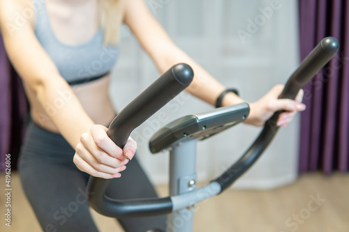 A beautiful athletic girl is engaged on an exercise bike in front of the window at home, front view, close-up. the concept of exercising or losing weight