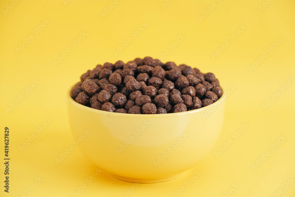 Chocolate cereal corn balls in a yellow bowl on a yellow background. Copy, empty space for text Chocolate cereal corn balls in a yellow bowl on a yellow background. Copy, empty space for text