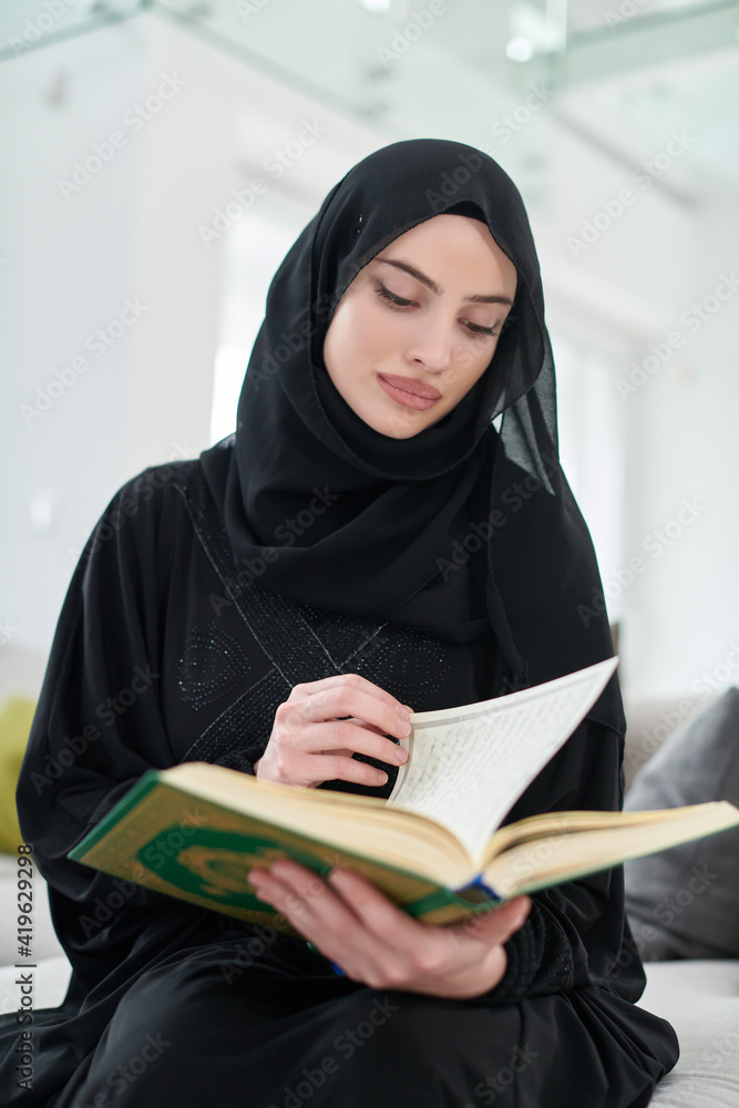 Portrait of young muslim woman reading Quran in modern home