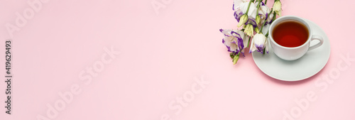 Purple flowers and a white coffee cup on a pink background. A beautiful banner with space to copy.