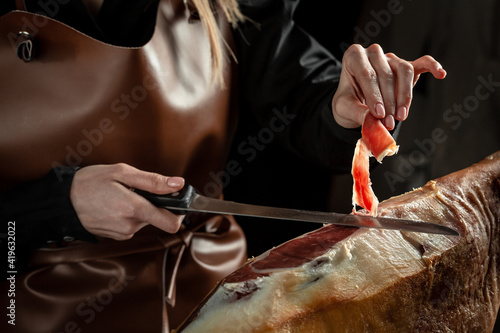 typical spanish salted ham. Slicing Spanish jamon iberico. Hands of a women cut a slice of traditionally spanish jamon