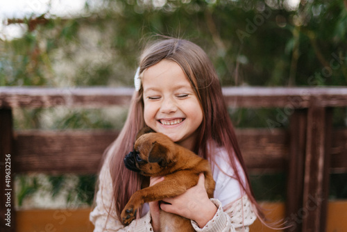 little girl laughs and holds a small dog in her arms