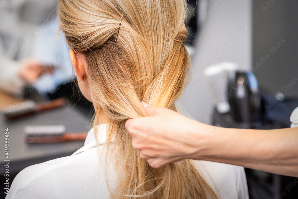 Fototapeta premium Close up of hands of female hairdresser styling hair of a blonde woman in a hair salon