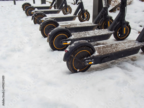 Electric urban transportation: the row of electric readies to ride scooter bikes with accumulators parked in the snow in winter.