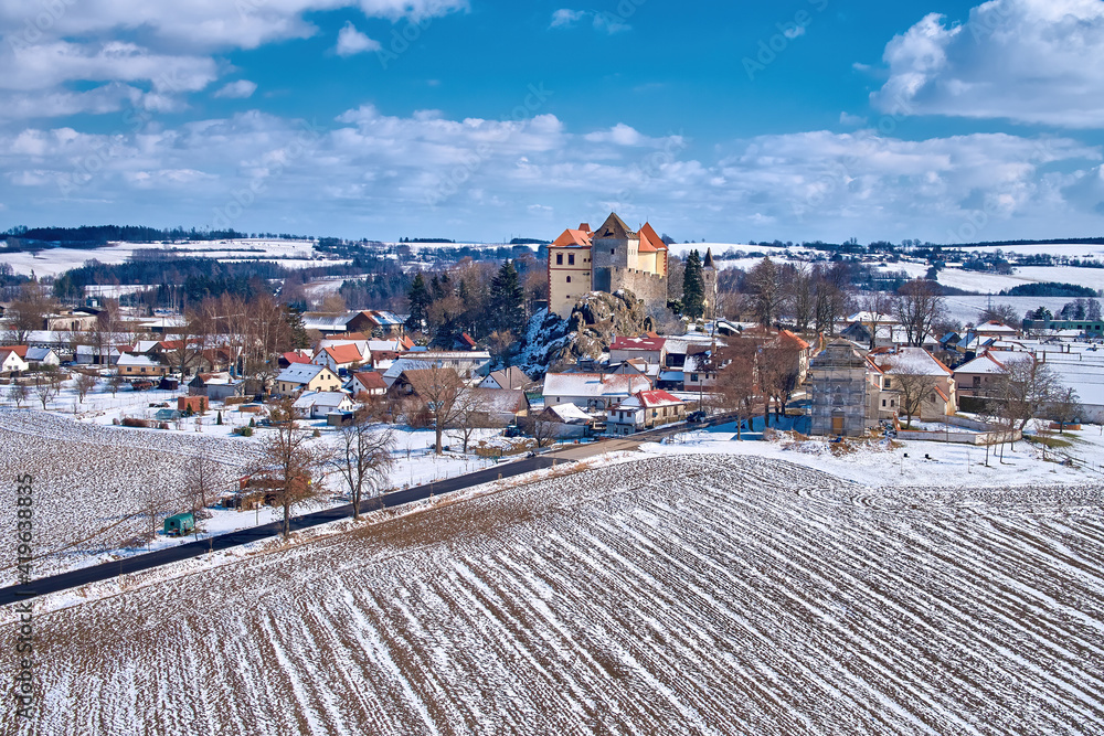 Winter, aerial view of Kamen castle covered in snow, illuminated by sun. Castle known from Hussite wars, built on  granite rock against blue sky with white clouds. Travel point, Czech landscape.