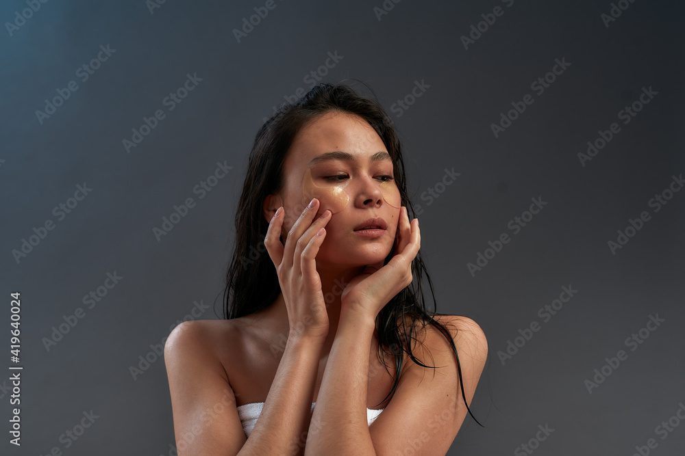 Young sensual beautiful asian woman touching eye patches with fingers of two hands and pressing them tighter to skin Young sensual beautiful asian woman touching eye patches with fingers of two hands and pressing them tighter to skin