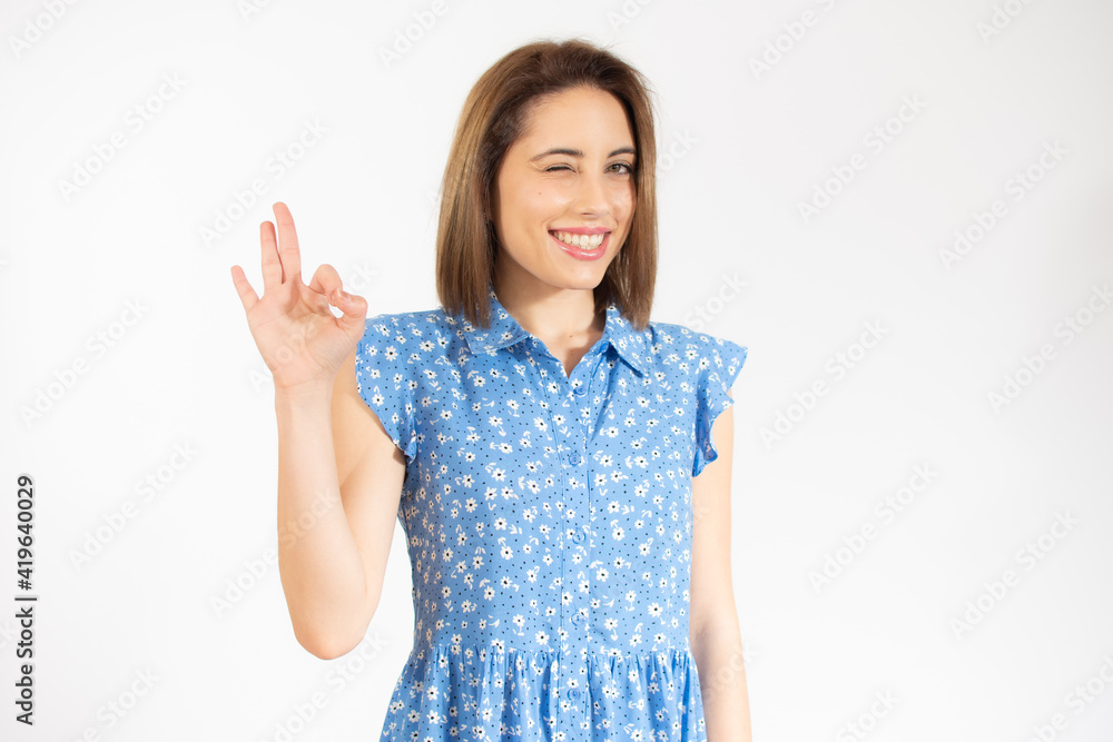 Young beautiful woman wearing casual dress standing over white isolated background smiling positive doing okay sign with hand and fingers. Successful expression. Young beautiful woman wearing casual dress standing over white isolated background smiling positive doing okay sign with hand and fingers. Successful expression.