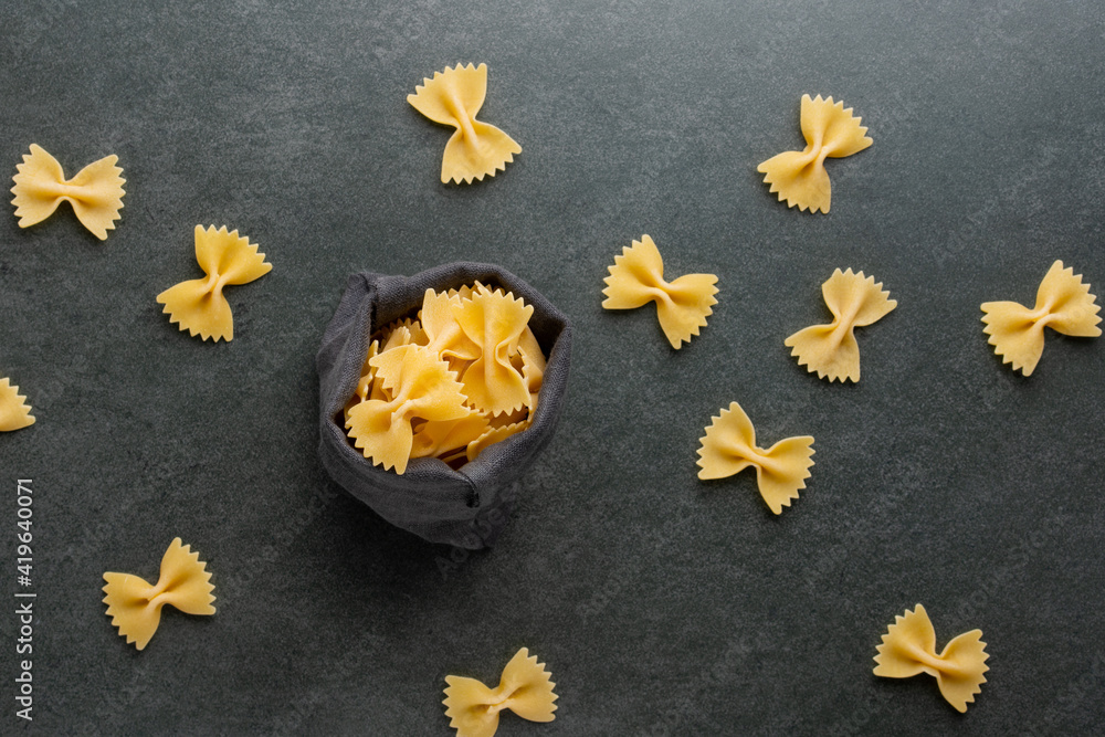Small linen bag full of pasta farfalle on dark background. Top view. Small linen bag full of pasta farfalle on dark background. Top view.