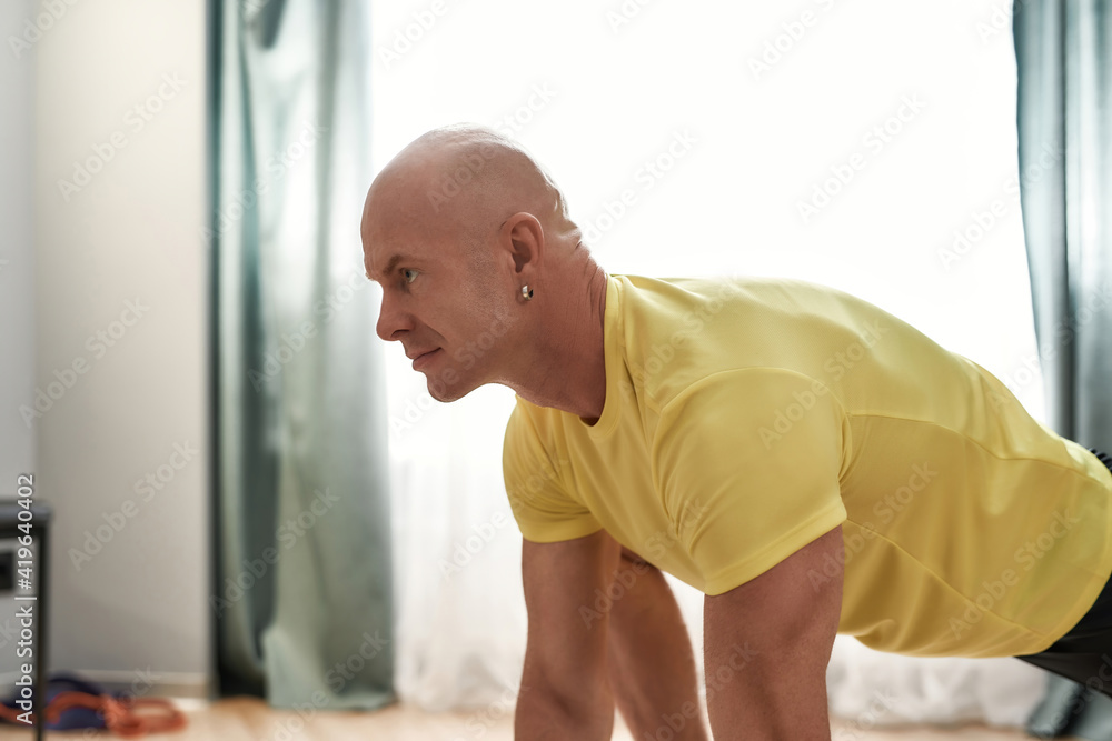 Fototapeta premium Sportive bald man looking focused while working out in living room at home on a daytime