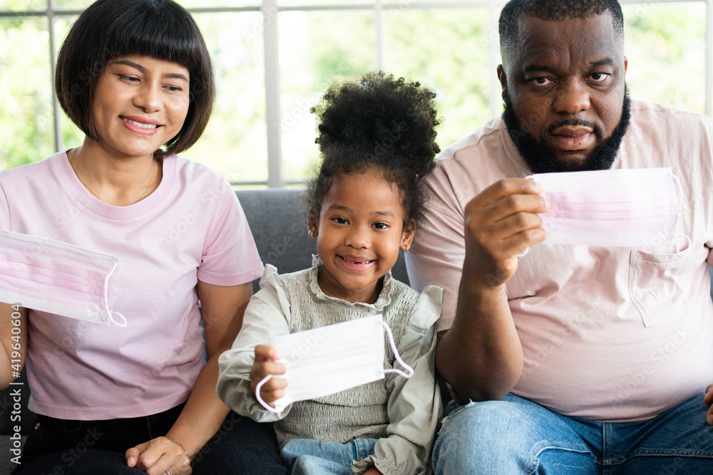 Mixed Race family sitting on the sofa and wearing medical face masks for against coronavirus world pandemic and stay quarantined together at home social distancing new normal lifestyle Mixed Race family sitting on the sofa and wearing medical face masks for against coronavirus world pandemic and stay quarantined together at home social distancing new normal lifestyle