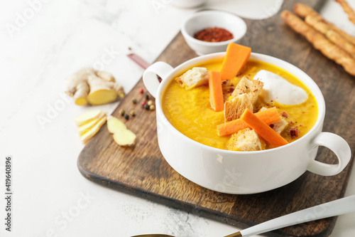 Cooking pot of fresh carrot cream soup on light background