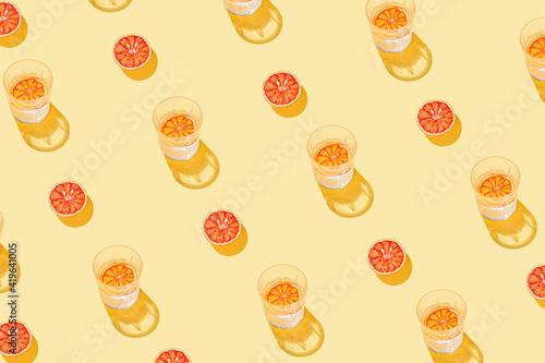 Creative pattern made with sliced grapefruit, blood orange and glass with lemonade or water on yellow background. Summer fruit and refreshment concept. Minimal style. Sunlit flat lay. Top view