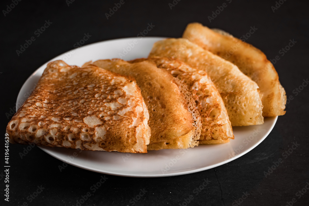 Tasty crepes on a plate on a black background. Traditional Russian food. Place for your text. Tasty crepes on a plate on a black background. Traditional Russian food. Place for your text.