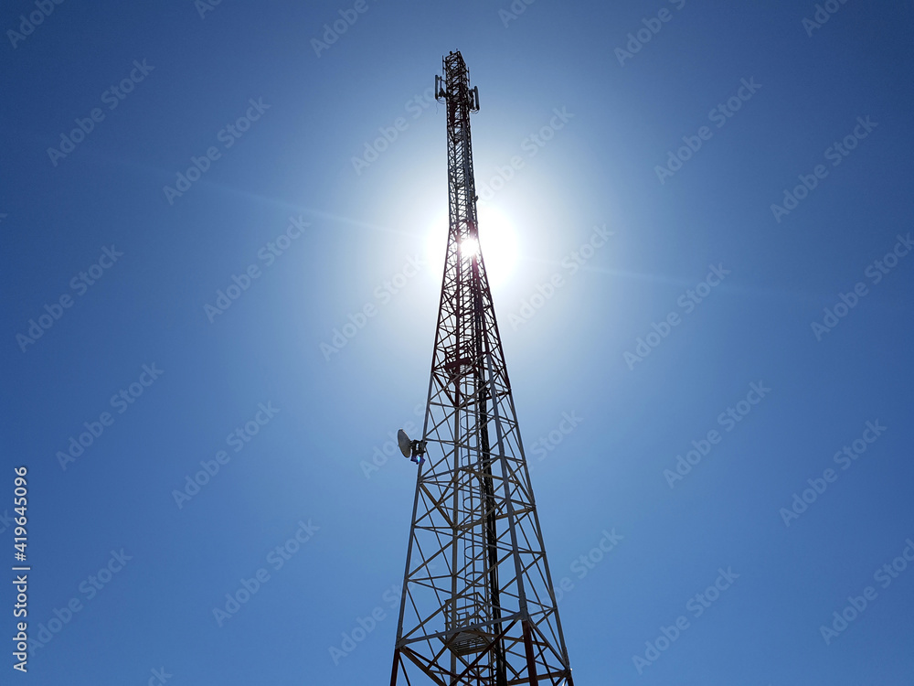 low angle view of cellular or mobile network tower against the sun in the blue sky. low angle view of cellular or mobile network tower against the sun in the blue sky.