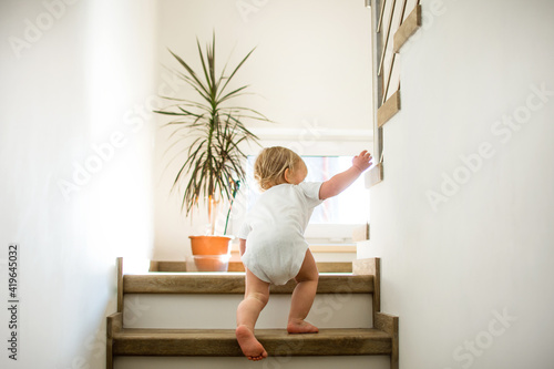 Little caucasian baby is crawling on stairs at home in sunny interior. Lifestile photography. Child, danger and safety at home.