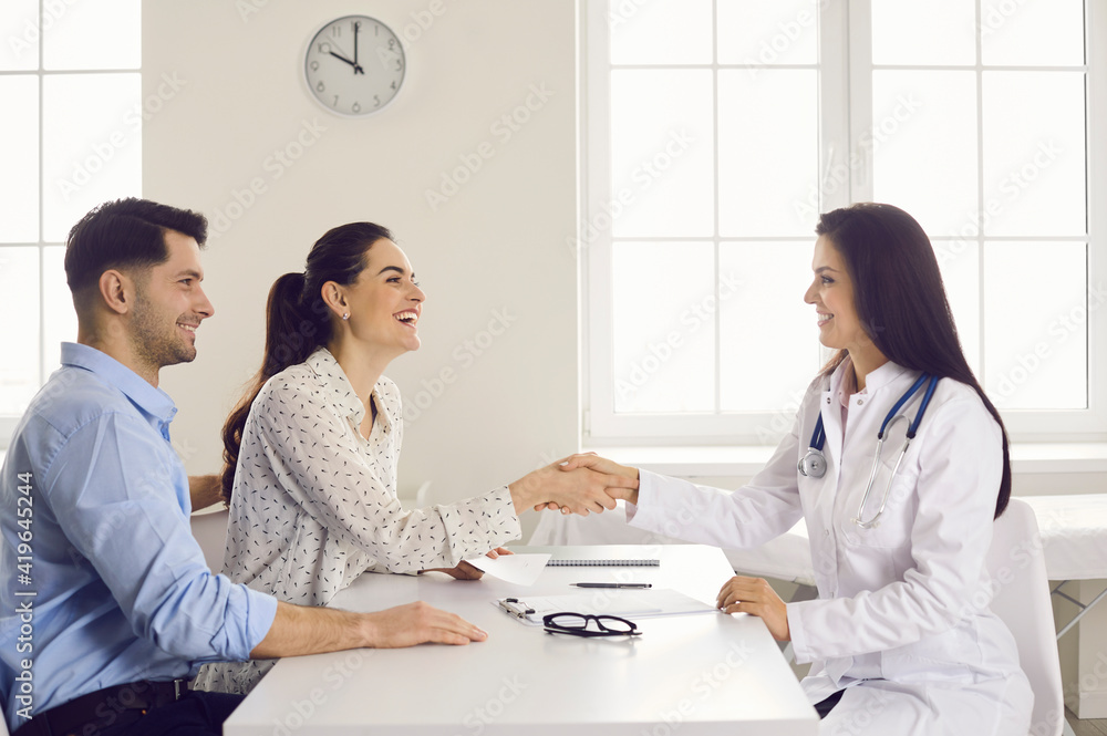 Happy woman patient giving gratitude handshake to doctor get good news about pregnancy on appointment at clinic office. Satisfied caucasian family couple visit physician for healthcare consultation Happy woman patient giving gratitude handshake to doctor get good news about pregnancy on appointment at clinic office. Satisfied caucasian family couple visit physician for healthcare consultation