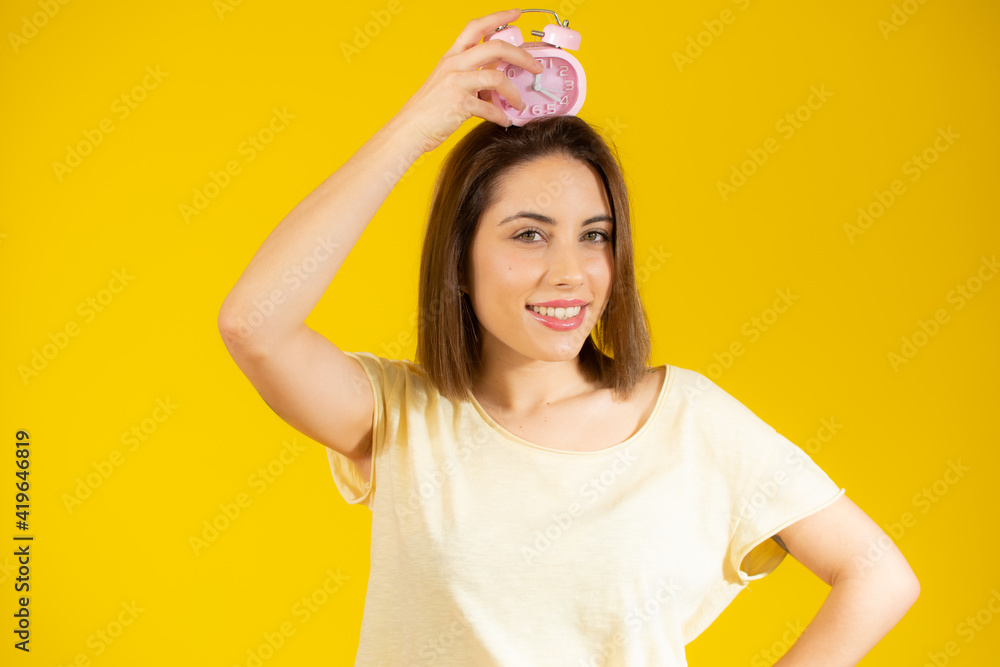 Portrait of cheerful young woman holding alarm clock isolated over yellow background Portrait of cheerful young woman holding alarm clock isolated over yellow background