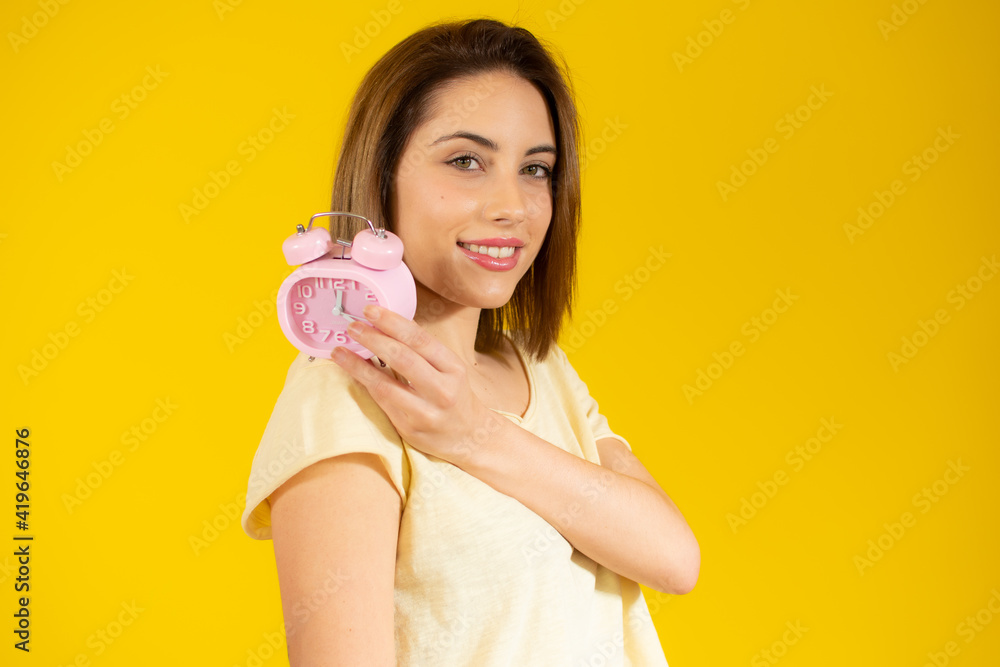 Portrait of cheerful young woman holding alarm clock isolated over yellow background Portrait of cheerful young woman holding alarm clock isolated over yellow background