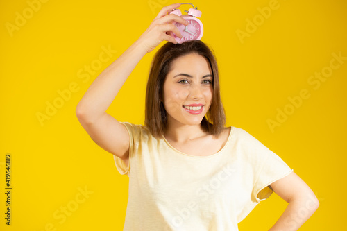 Portrait of cheerful young woman holding alarm clock isolated over yellow background