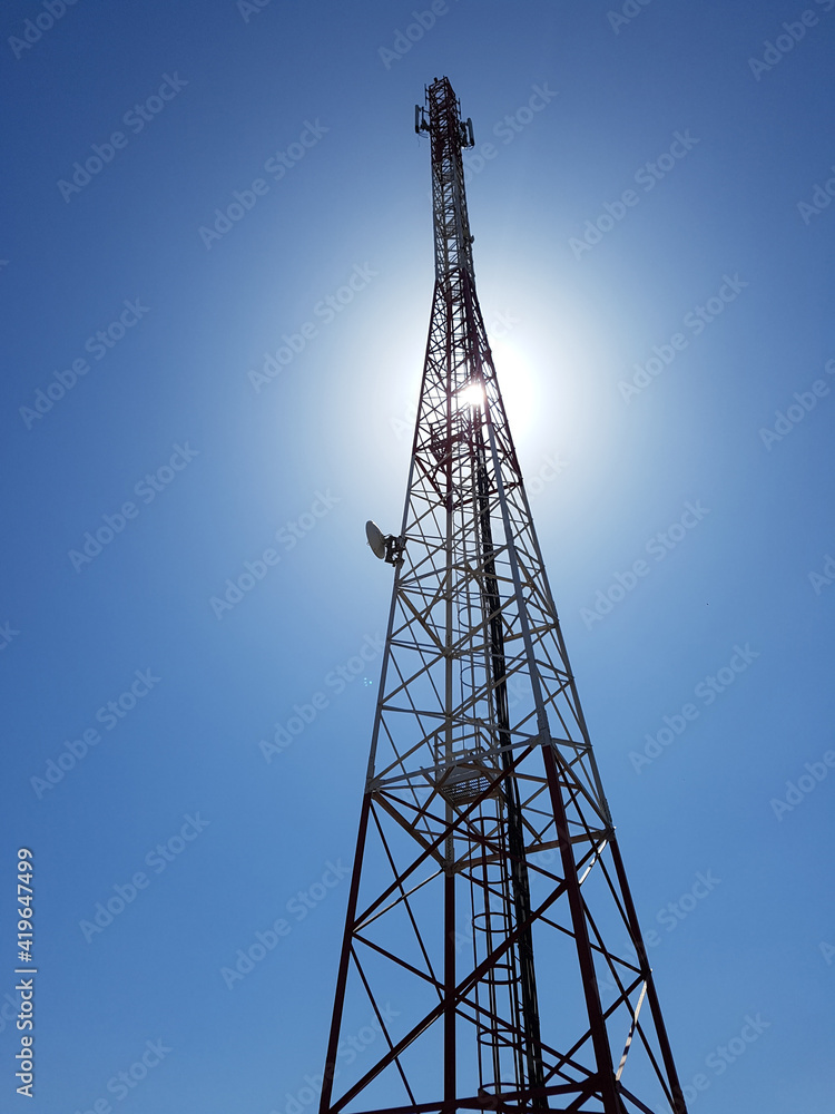 vertical low angle view of cellular or mobile network tower against the sun in the blue sky. vertical low angle view of cellular or mobile network tower against the sun in the blue sky.