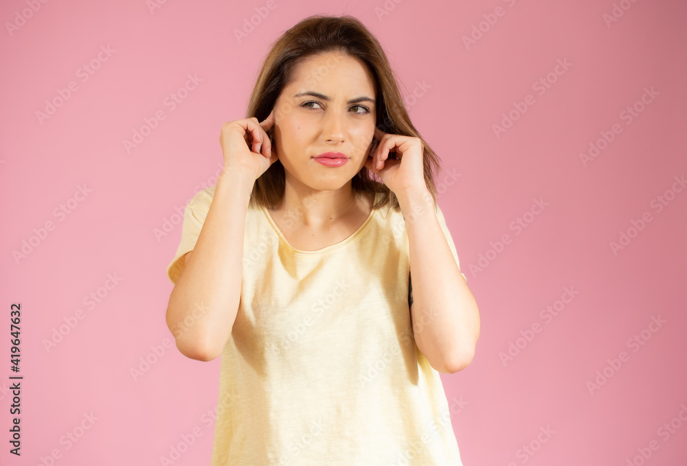 Young beautiful woman wearing casual t-shirt standing over isolated pink background covering ears with fingers with annoyed expression. Deaf concept. Young beautiful woman wearing casual t-shirt standing over isolated pink background covering ears with fingers with annoyed expression. Deaf concept.