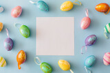 Colorful Easter eggs on pastel blue background. Easter decoration, white card with space for text. Top view, flat lay, copy space