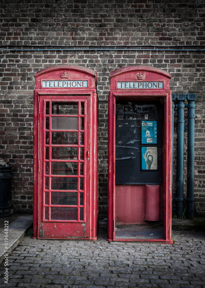 Two vintage and weathered red telephone boxes against a brick wall on a cobbled London street
