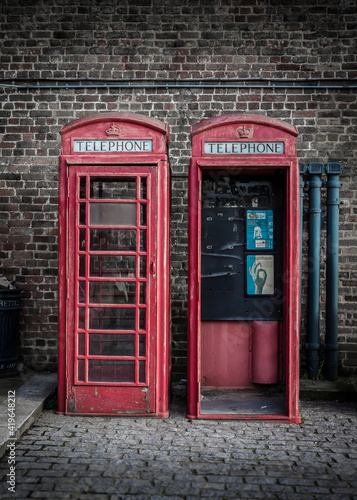 Two vintage and weathered red telephone boxes against a brick wall on a cobbled London street