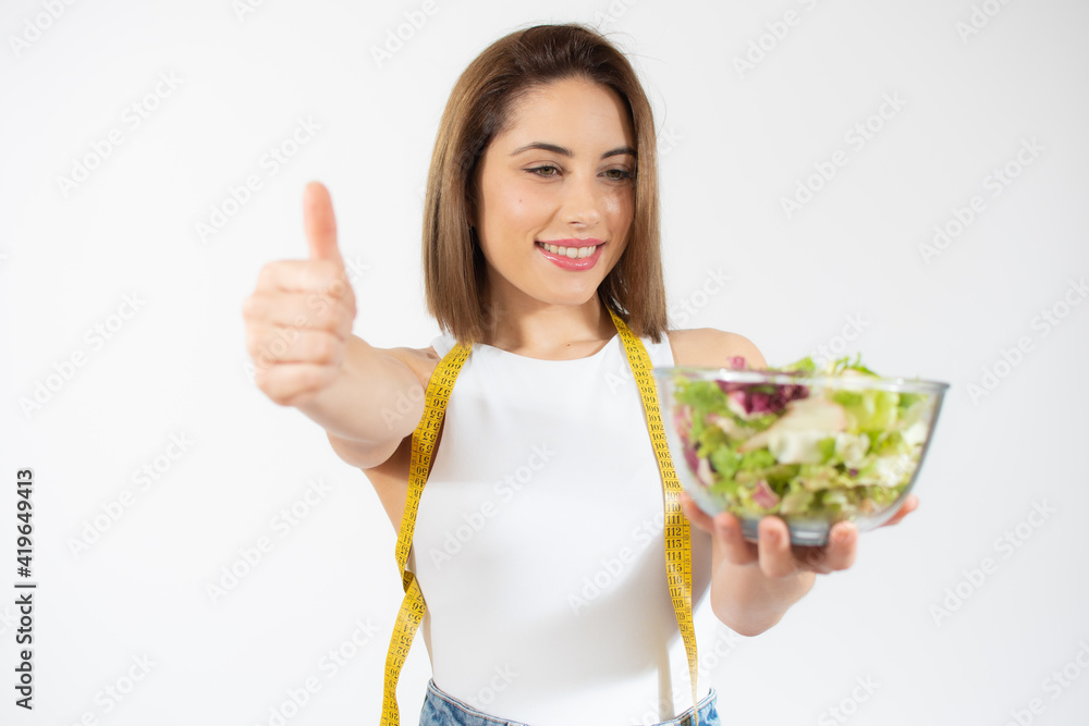 Young woman with measure tape showing a bowl of salad isolated over white background Young woman with measure tape showing a bowl of salad isolated over white background