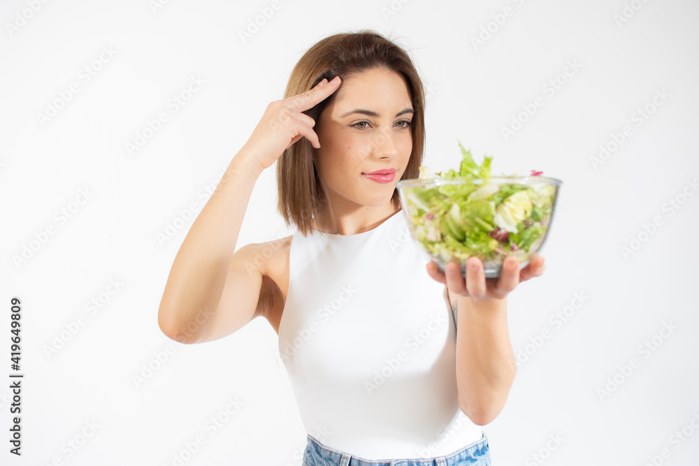 Young pensive woman showing a bowl of salad isolated over white background Young pensive woman showing a bowl of salad isolated over white background