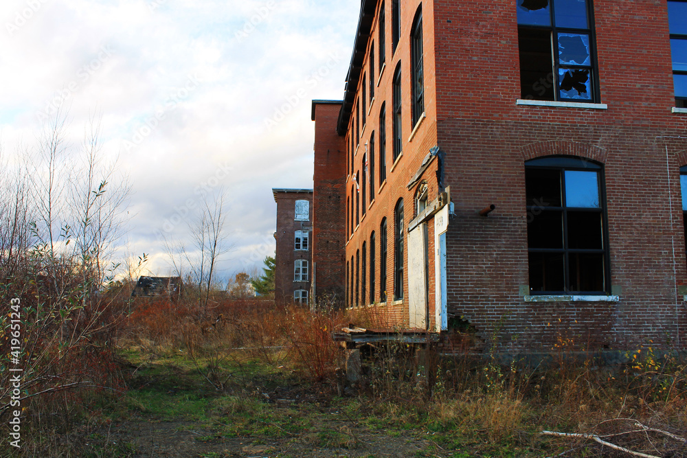 An old, abandoned, brick building that is falling into ruin, with broken windows and overgrown yard.