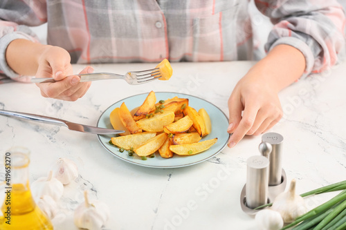 Woman eating tasty baked potato with garlic on light background