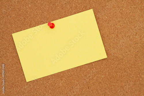 Retro yellow paper index card with pushpin on corkboard