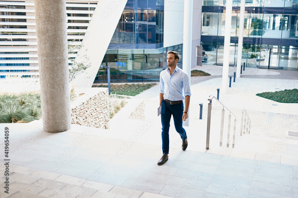 Confident young businessman walking up stairs outside of an office ...