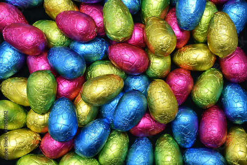 Pile or group of multi colored colourful foil wrapped chocolate easter eggs in pink, blue, yellow and lime green.
