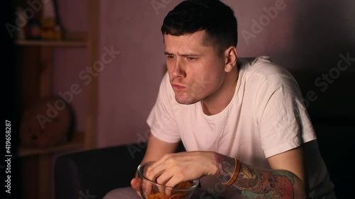A man sitting at coach and watching TV, eating fastfood