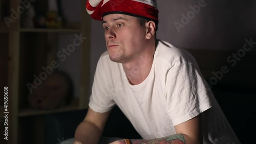 A man with strange hat watching a sport match on TV. Arguing with a screen, eating fastfood