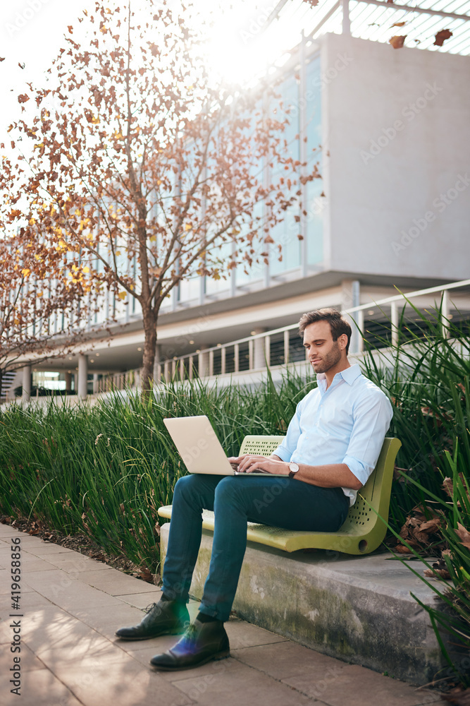 Young businessman working on a laptop outside on a bench Young businessman working on a laptop outside on a bench