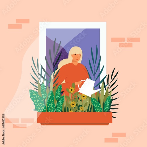 The girl is watering the plants. A girl with long hair stands near the window with a watering pad and watering the plants in a flowerpot on the balcony