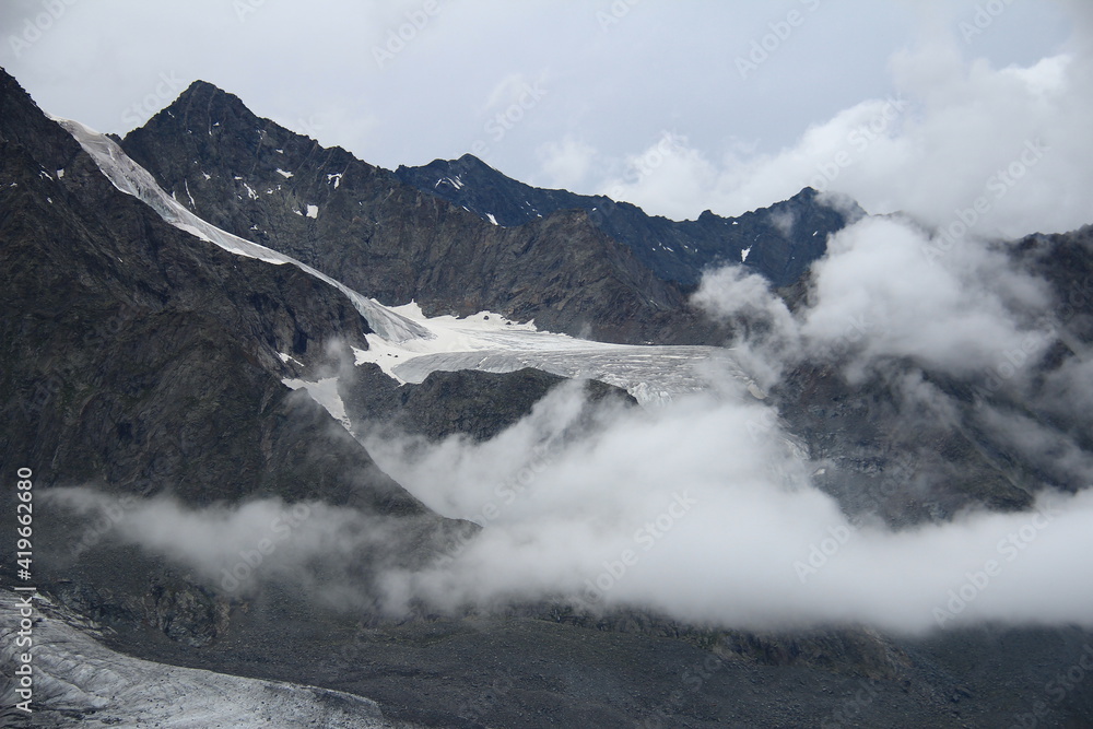 Alpine rocky ridge with glaciers, low clouds, satellites of Mount Belukha, stone mountains, rocky mountains with peaked peaks, cloudy, Ak-Kem valley