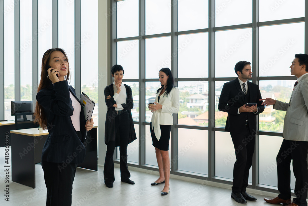 portrait of young asian businesswoman with smiling face stnading in office with background of multiethnic colleagues portrait of young asian businesswoman with smiling face stnading in office with background of multiethnic colleagues
